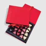 Image of Custom Candy Boxes - Open red gift box showcasing an assortment of heart-shaped chocolates in pink, white, and dark varieties. Perfect for Valentine's Day.