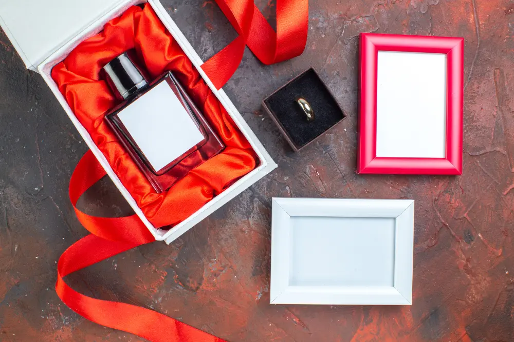 This photograph displays an open, elegant white rigid gift box. A red satin or silk fabric lines the inside, creating a luxurious contrast with the glass perfume bottle. The image highlights the "gift" aspect of the product, showing that the packaging is as important as the item itself. This kind of presentation demonstrates that rigid boxes elevate the perceived value and provide a premium unboxing experience for a perfume brand.